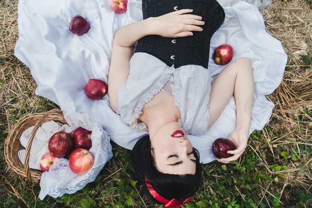 Snow White is laying in the floor, surrounded by red apples. She seems to be in a profound sleep.
