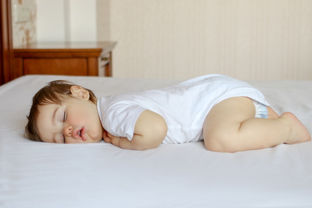 Funny baby sleeping on his stomach on bed at home. Child daytime bottom up sleeping position