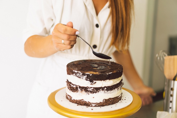 Confectioner girl is preparing a cake biscuit with white cream and chocolate. Cooking cakes.