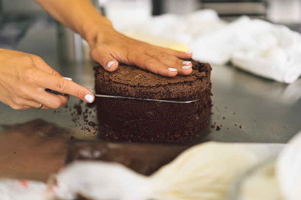 Confectioner girl is preparing a cake biscuit with white cream and chocolate. Cooking cakes.