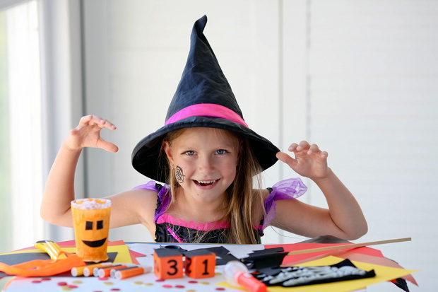 A little girl in a witch costume looks at the camera and scares.