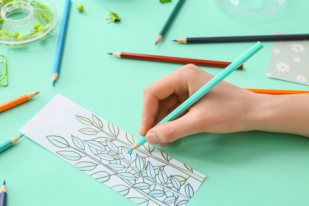 Woman coloring bookmark on color background