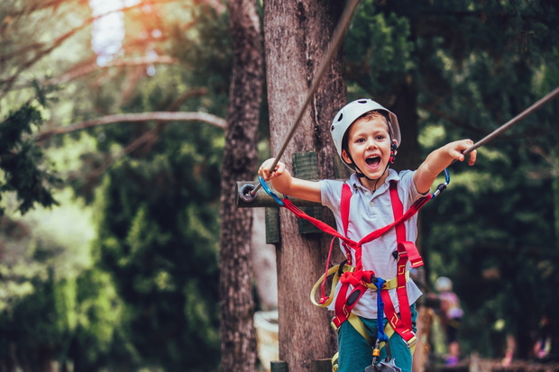 Little boy climbing in adventure activity park with helmet and s