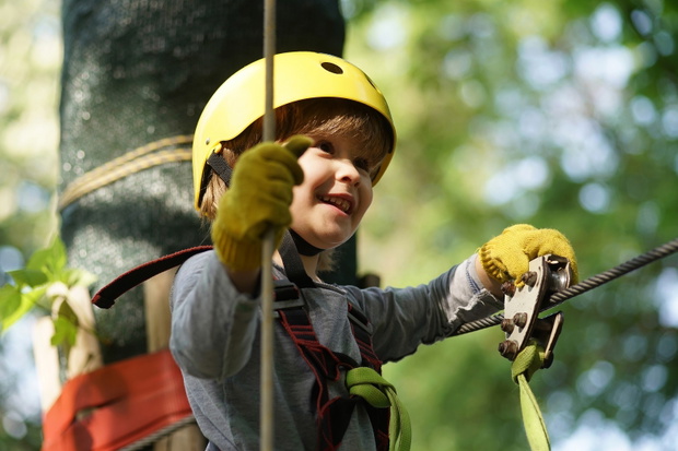 Climber child on training. Cute little boy in climbing safety equipment in a tree house or in a rope park climbs the rope. Safe Climbing extreme sport with helmet