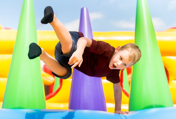 Child jumping on colorful playground trampoline. Kids jump in inflatable bounce castle on kindergarten birthday party Activity and play center for young child. Little girl playing outdoors in summer.