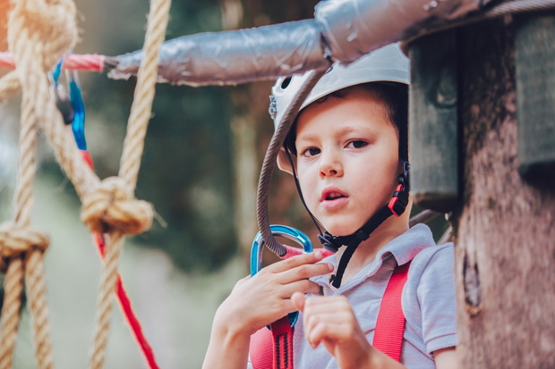 Little boy climbing in adventure activity park with helmet and s