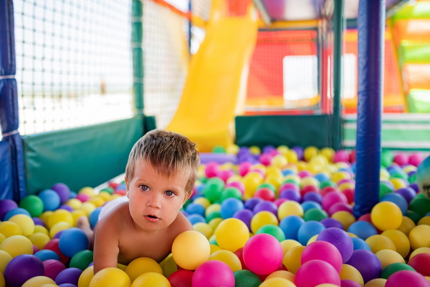 The kid plays in the playroom and rolls down the slide into the pool with small balls