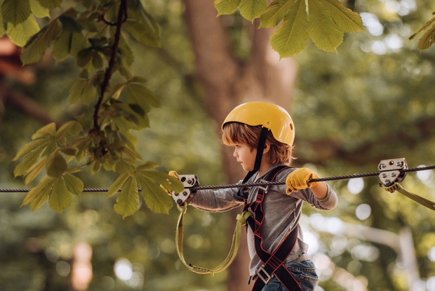 Happy child climbing in the trees. Children summer activities. Early childhood development. Child. Safe Climbing extreme sport with helmet.