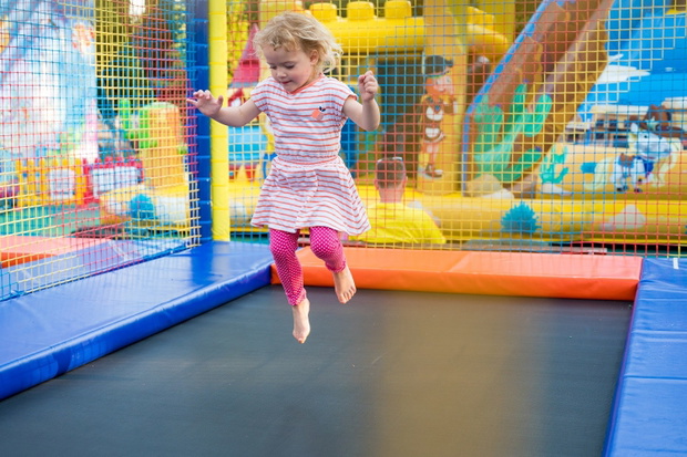 Cute blonde girl jumping on big trampoline at outdoor playground.