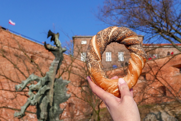 Woman hand holding Cracow's bagel on the Wawel Dragon background
