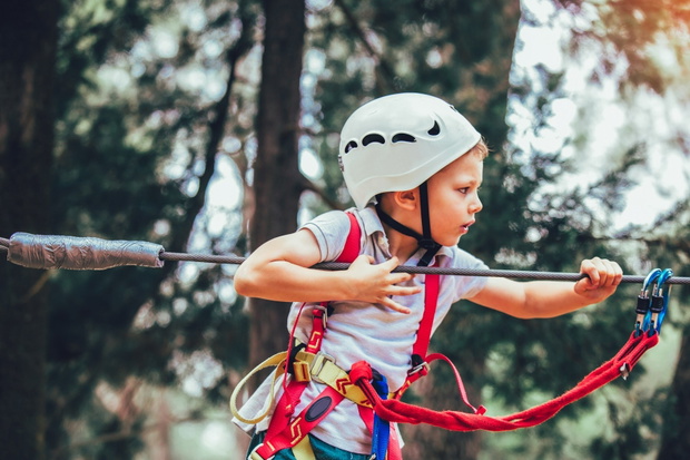 Little boy climbing in adventure activity park with helmet and s