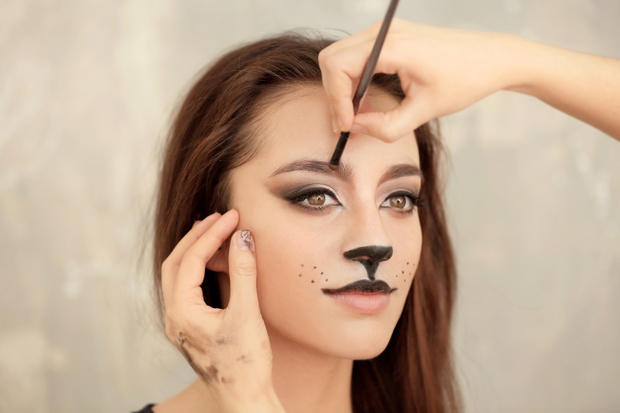 Visagiste applying cat makeup onto face of beautiful young woman