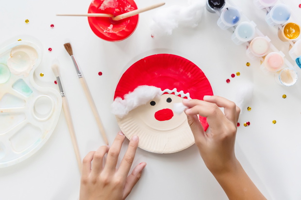 The child glues the parts Santa made from paper plate. Handmade. Project of children's creativity, handicrafts, crafts for kids. Preparation for christmas. Decoration.