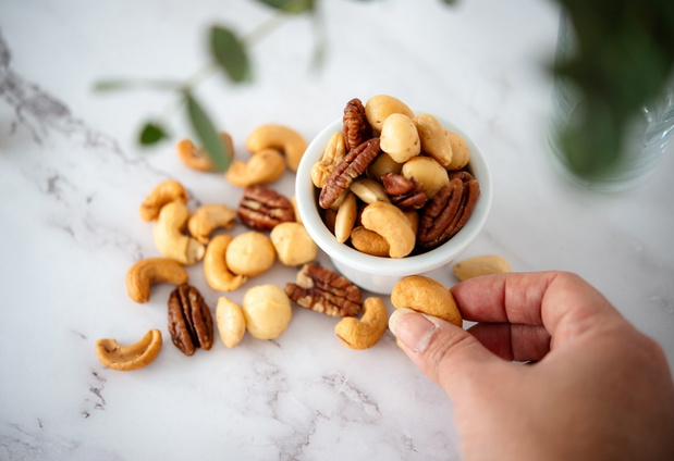 A hand of a young woman holding nut, eating mixed nuts alone in the kitchen healthy snack to fill energy before fitness concept