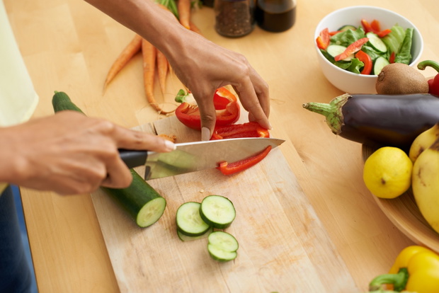 Closeup, hands and cutting with vegetables, nutrition and plant based diet in a kitchen. Person, home and cooking health food, lunch and vegan meal with variety, vitality and weight loss with knife