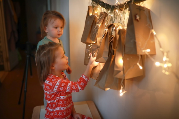 Christmas waiting calendar for children from paper bags and tree branches. Brother and sister together are looking for package with gift on Advent calendar.