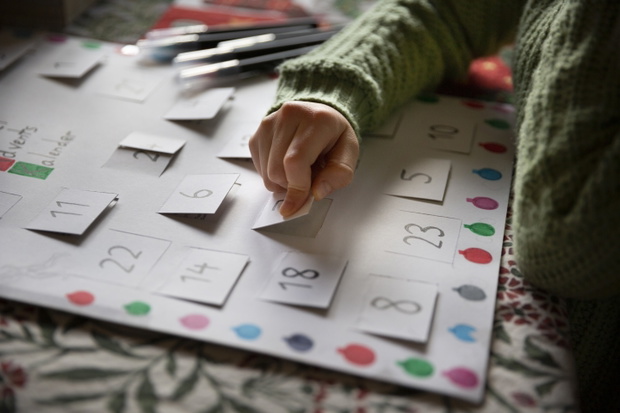 Close up of a child opening the window of a simple, homemade, card Advent Calendar on a dining table