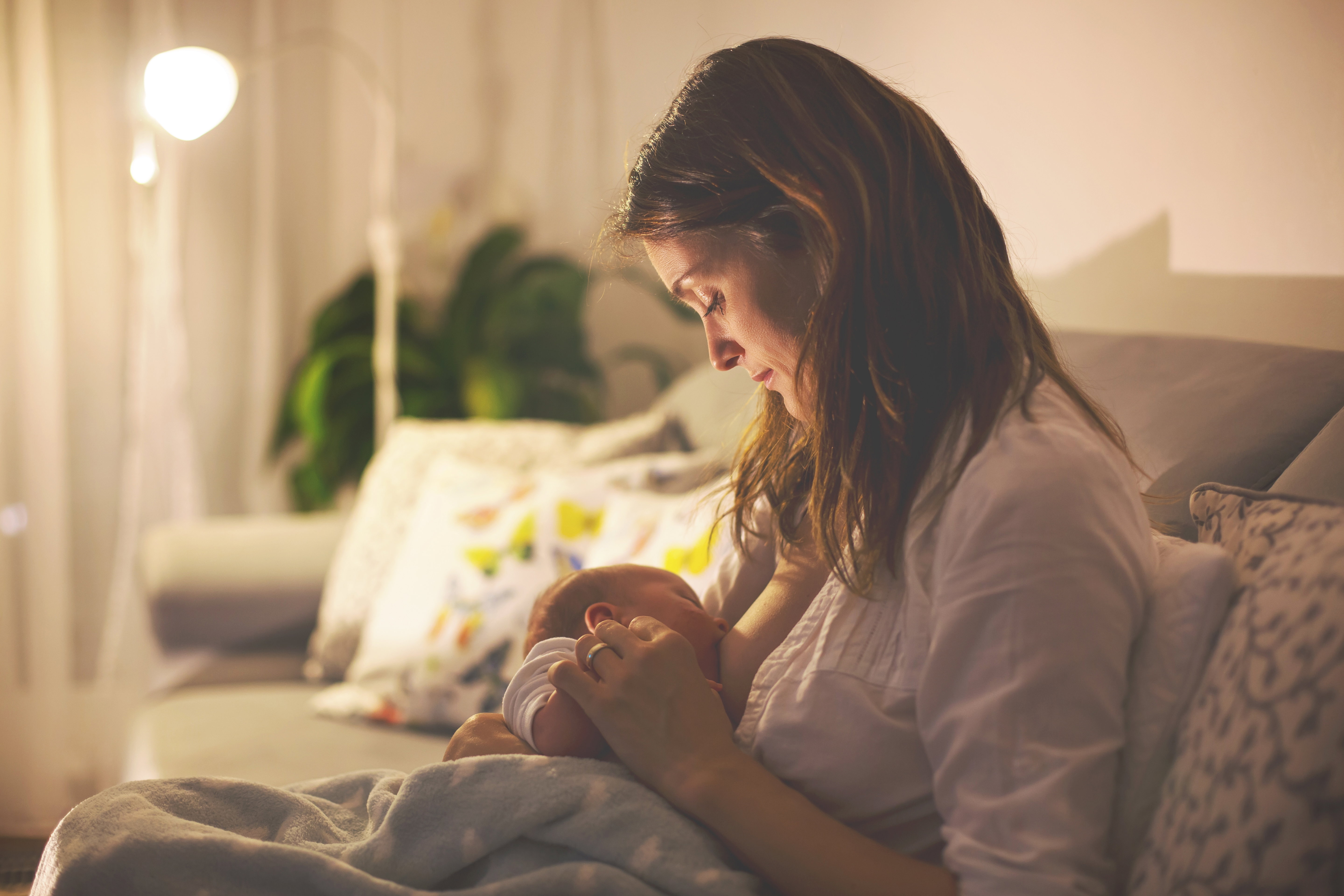 Young beautiful mother, breastfeeding her newborn baby boy at night
