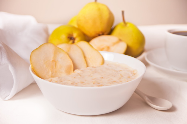 Oatmeal porridge with ripe pears in the white bowl, a bowl of pears and cup of coffee on the background. Health breakfast. Close up.