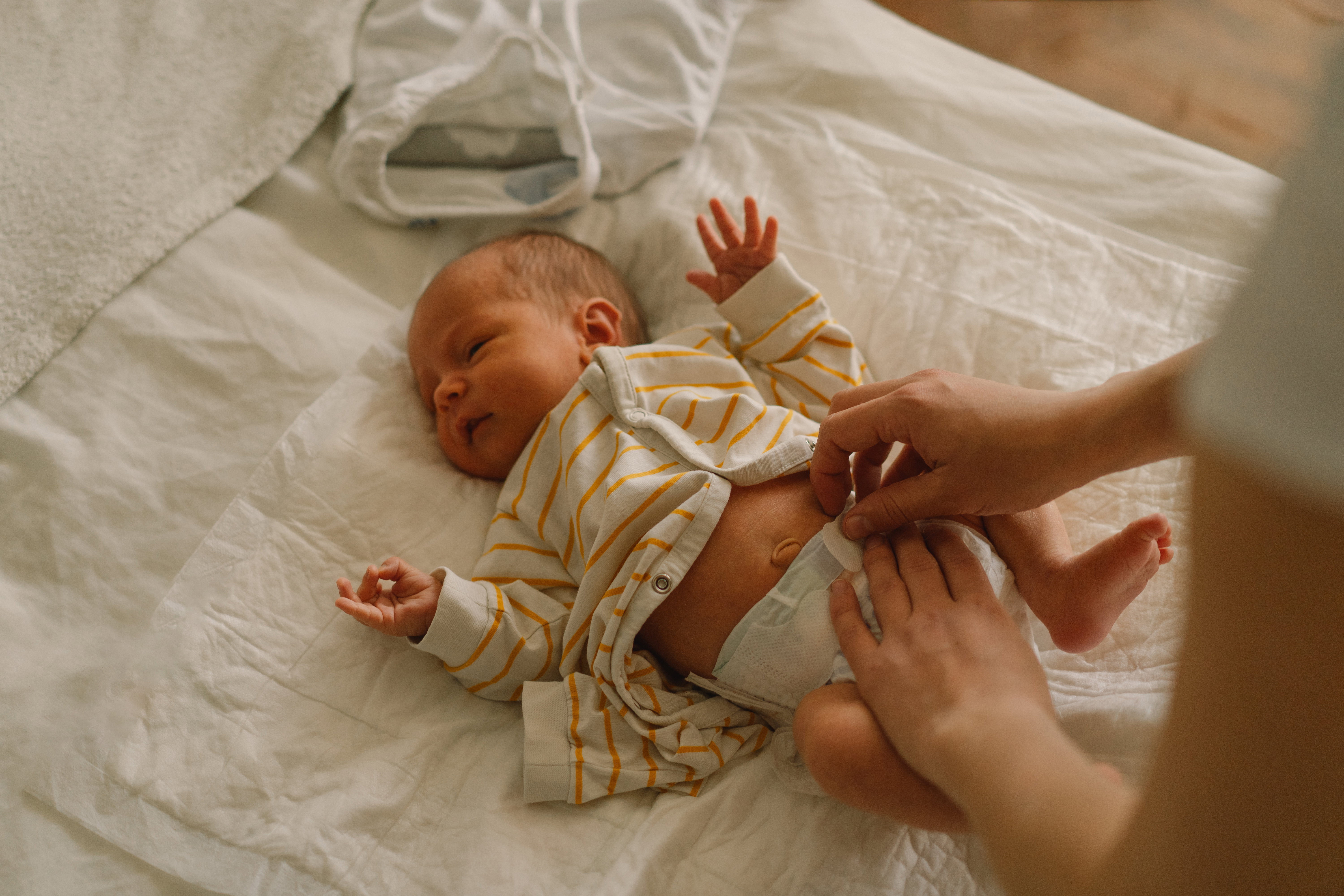 Happy young mother playing with baby while changing his diaper on bed.