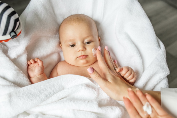 Mother applies moisturizer for healthy skin care on cute baby face. Skin care lotion for children.