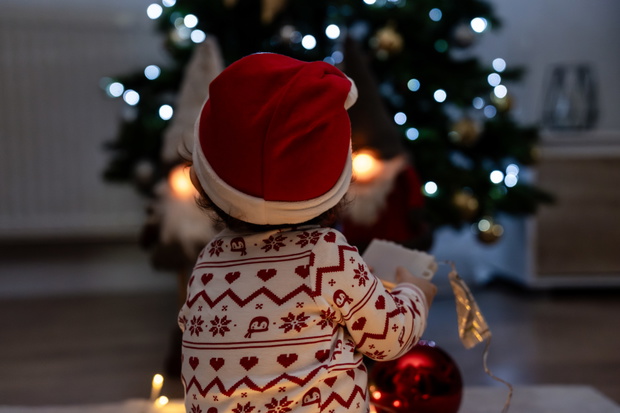Baby wearing christmas clothes holding wish list near christmas tree