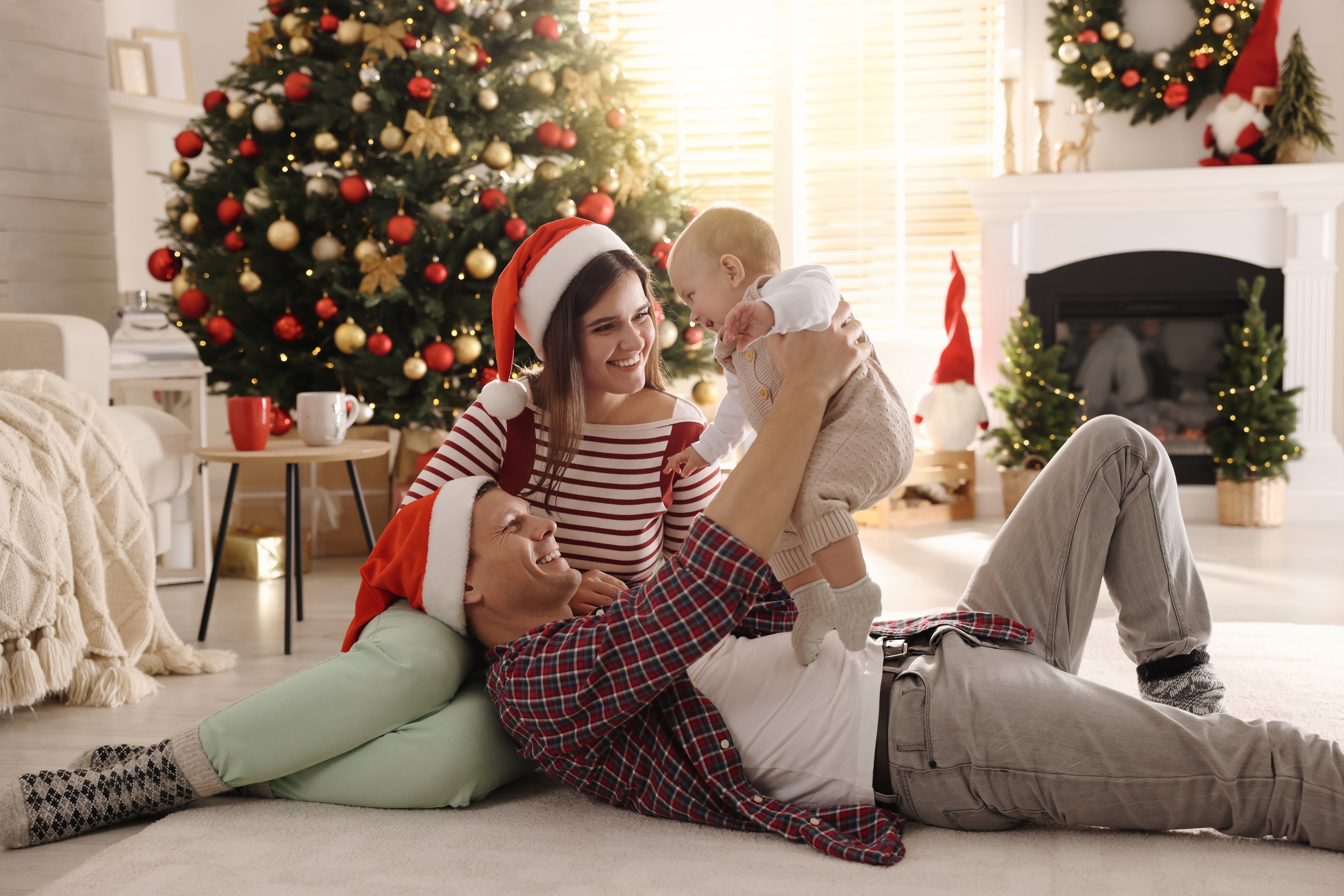 Happy family with cute baby on floor in room decorated for Christmas