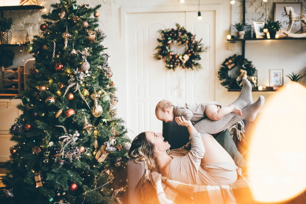 Happy mother and little boy playing near Christmas tree at home. Mom and son relaxing in house with winter decoration.