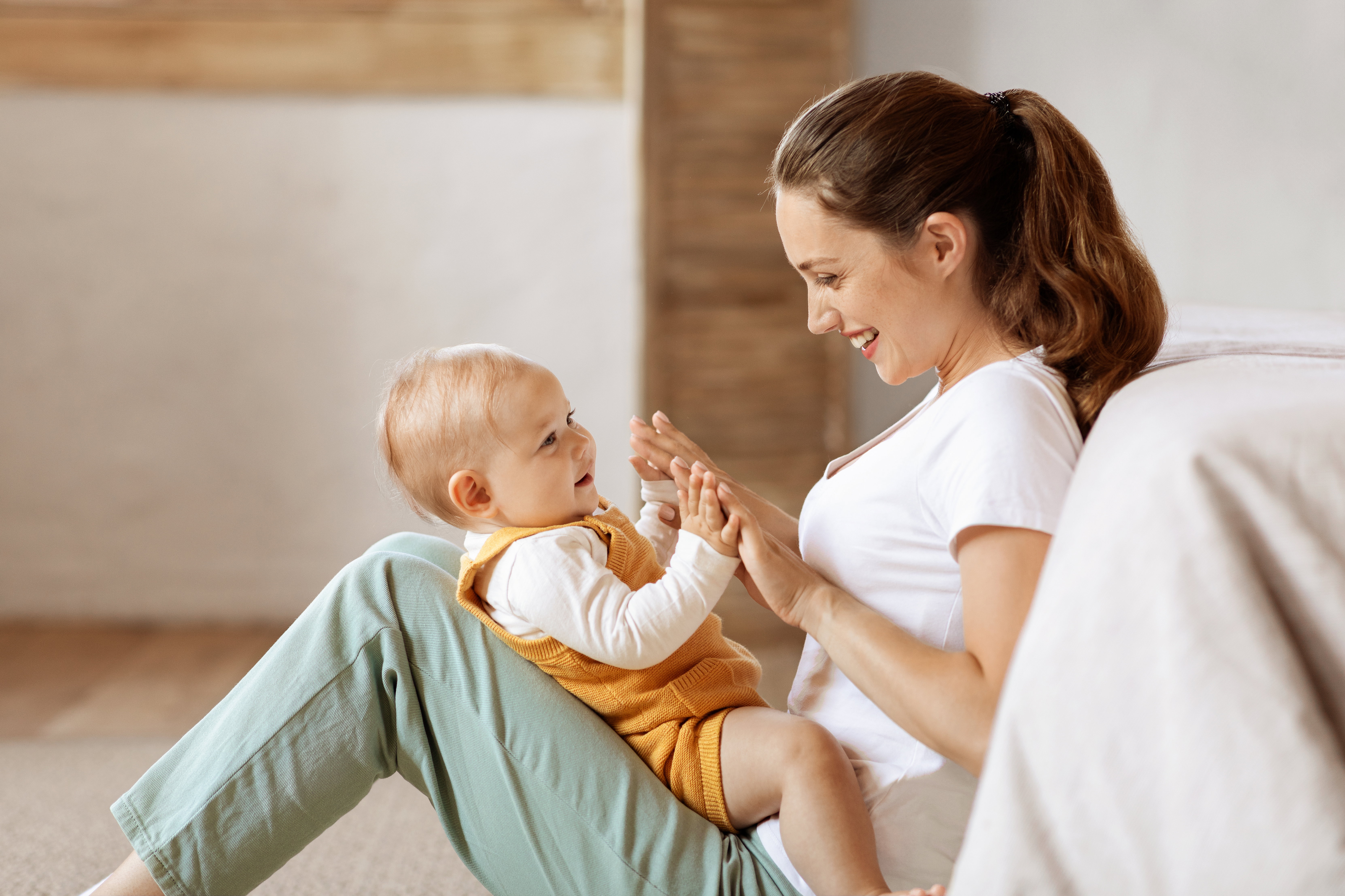 Loving young mother caressing her cute baby boy, home interior