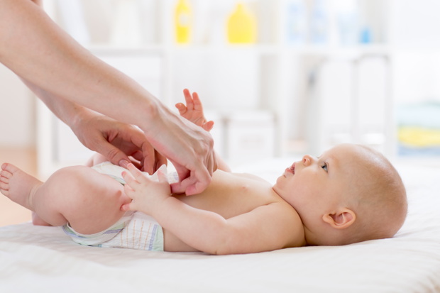 Woman putting diaper on her happy baby on bed in nursery
