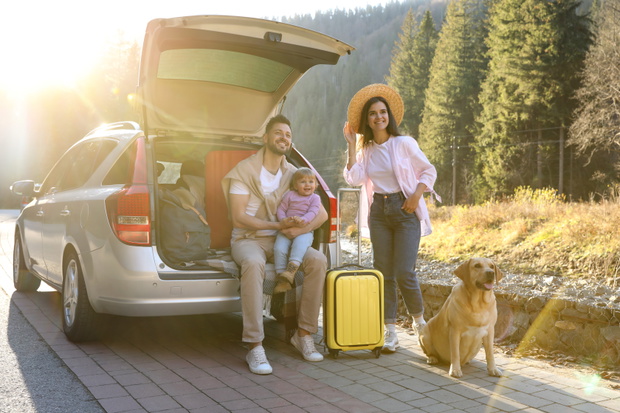 Parents, their daughter and dog near car outdoors. Family traveling with pet