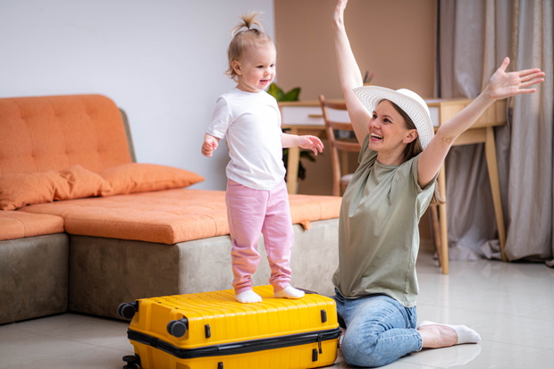 Happy Mother and baby girl with yellow suitcase baggage and clothes, family ready for traveling on vacation at home