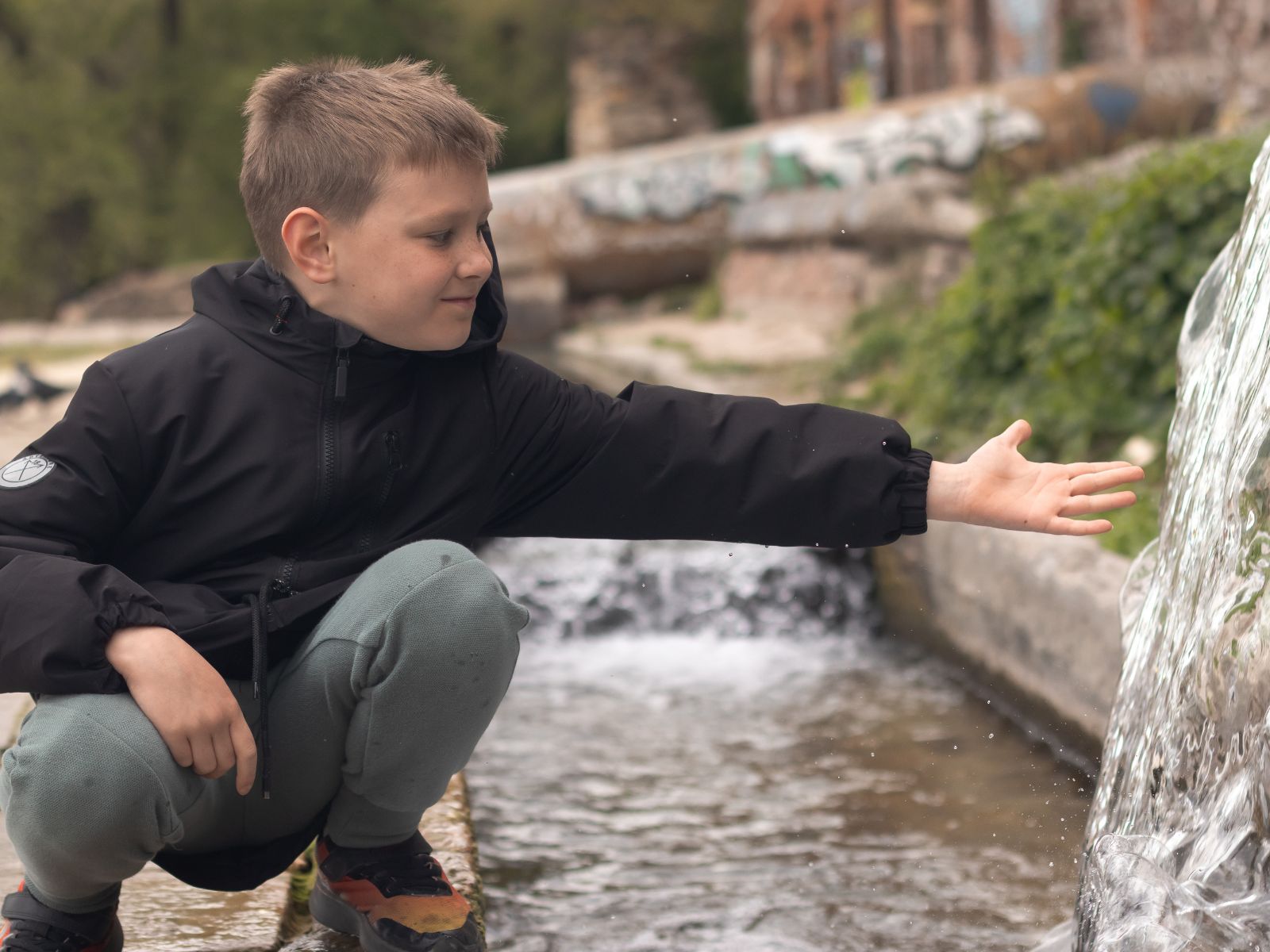 chłopiec w czarnej kurtce nad małym potokiem
