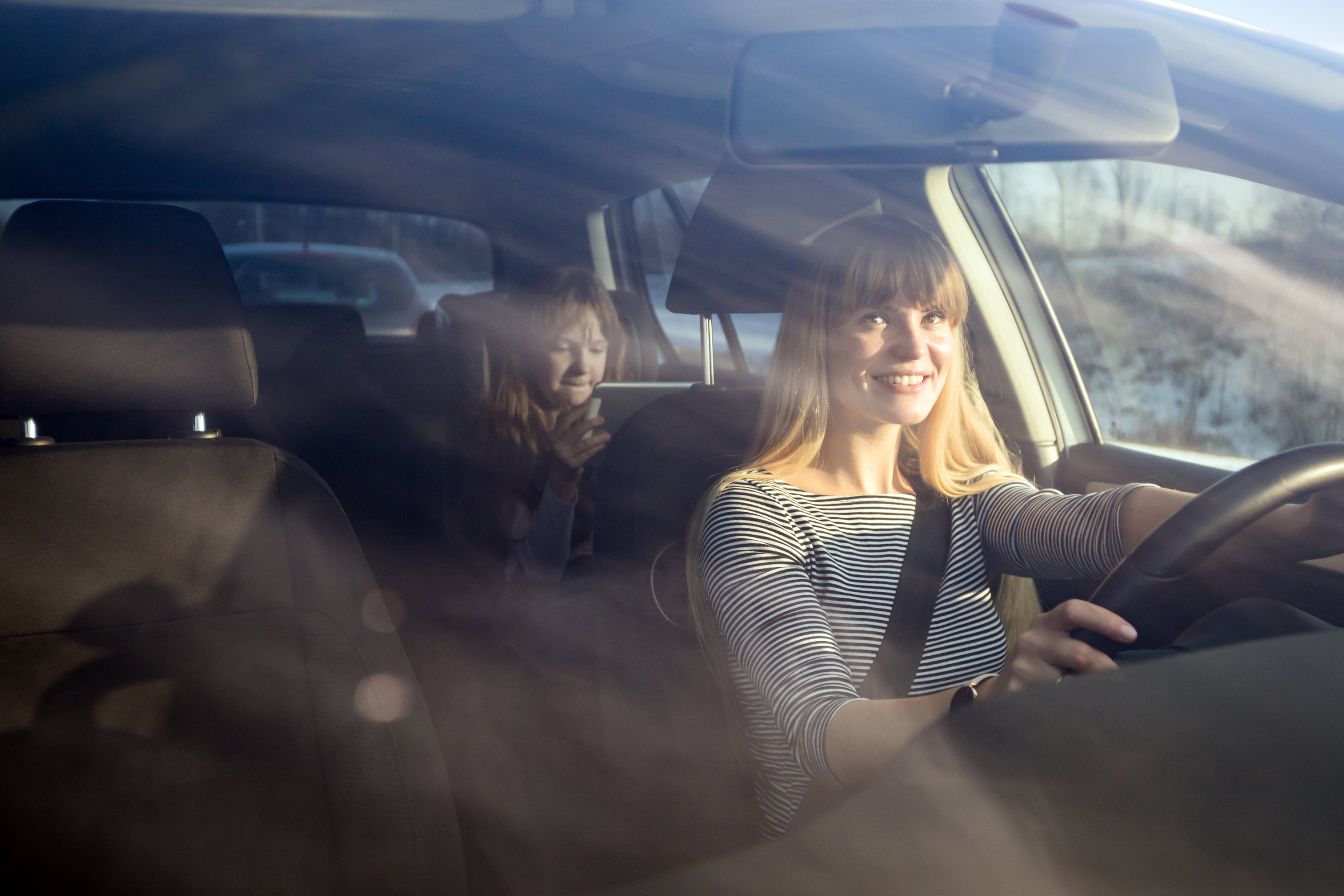 Mom driving car while her daughter sitting on back seat and using digital tablet