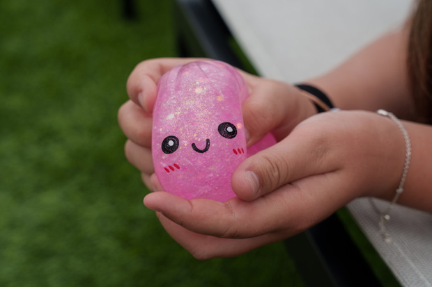 Close-up of a child squeezing a pink glitter squishy toy with smiling face, highlighting sensory play, relaxation, tactile stimulation, and fine motor development