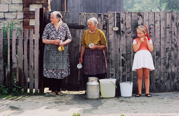Two senior women and girl by fence in front of house with buckets