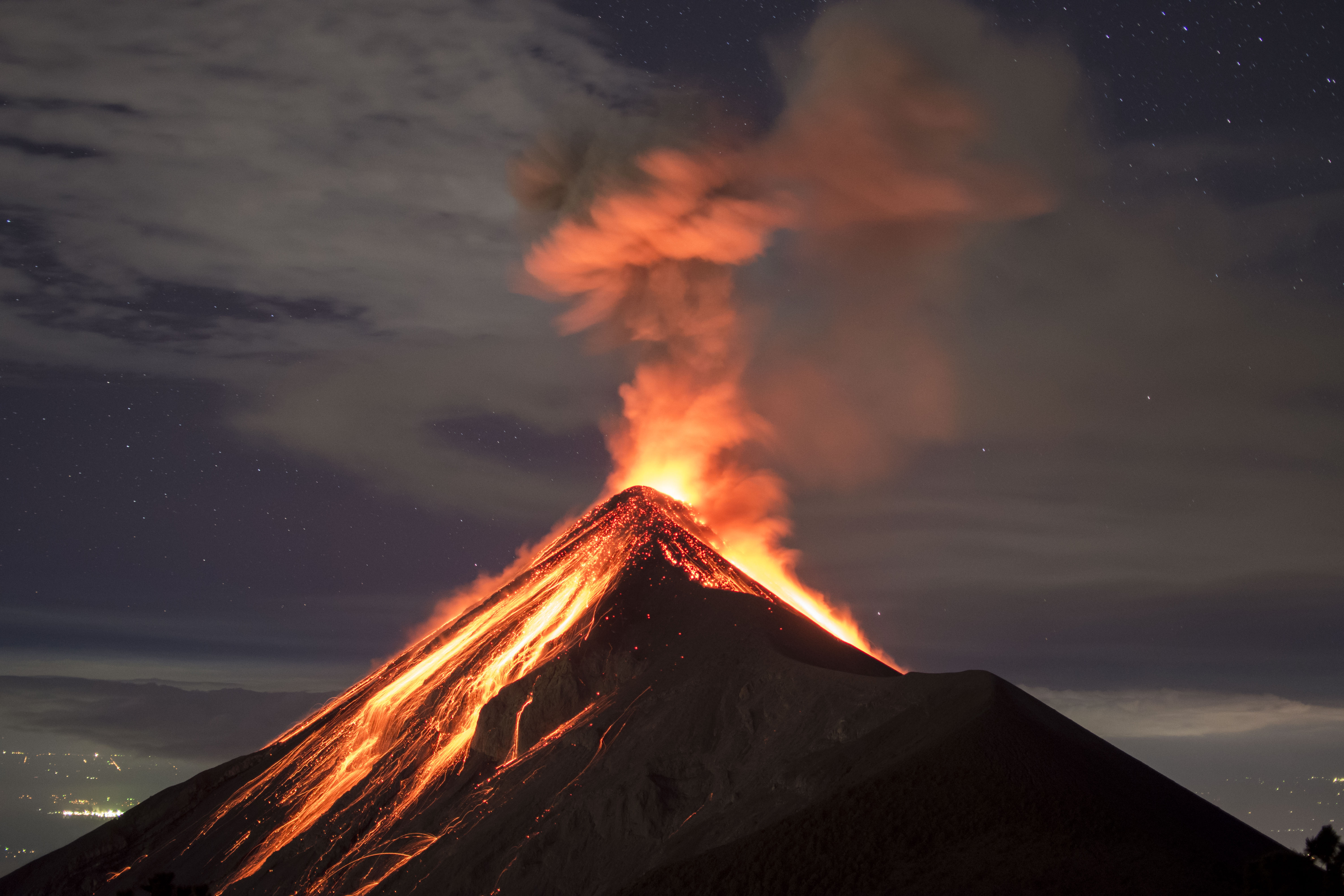 Erupcja wulkanu Fuego nocą, widziana z Acatenango. W kadrze lawa, gwiazdy i światła miasta w tle.