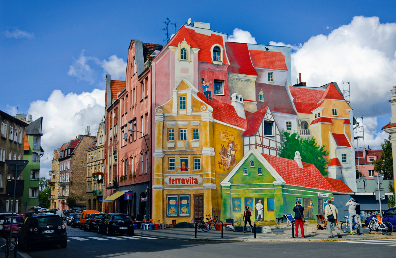 Przed sobą ma się mural z trębaczem i kotem, za sobą zabytkowy gotycki kościół św. Małgorzaty.