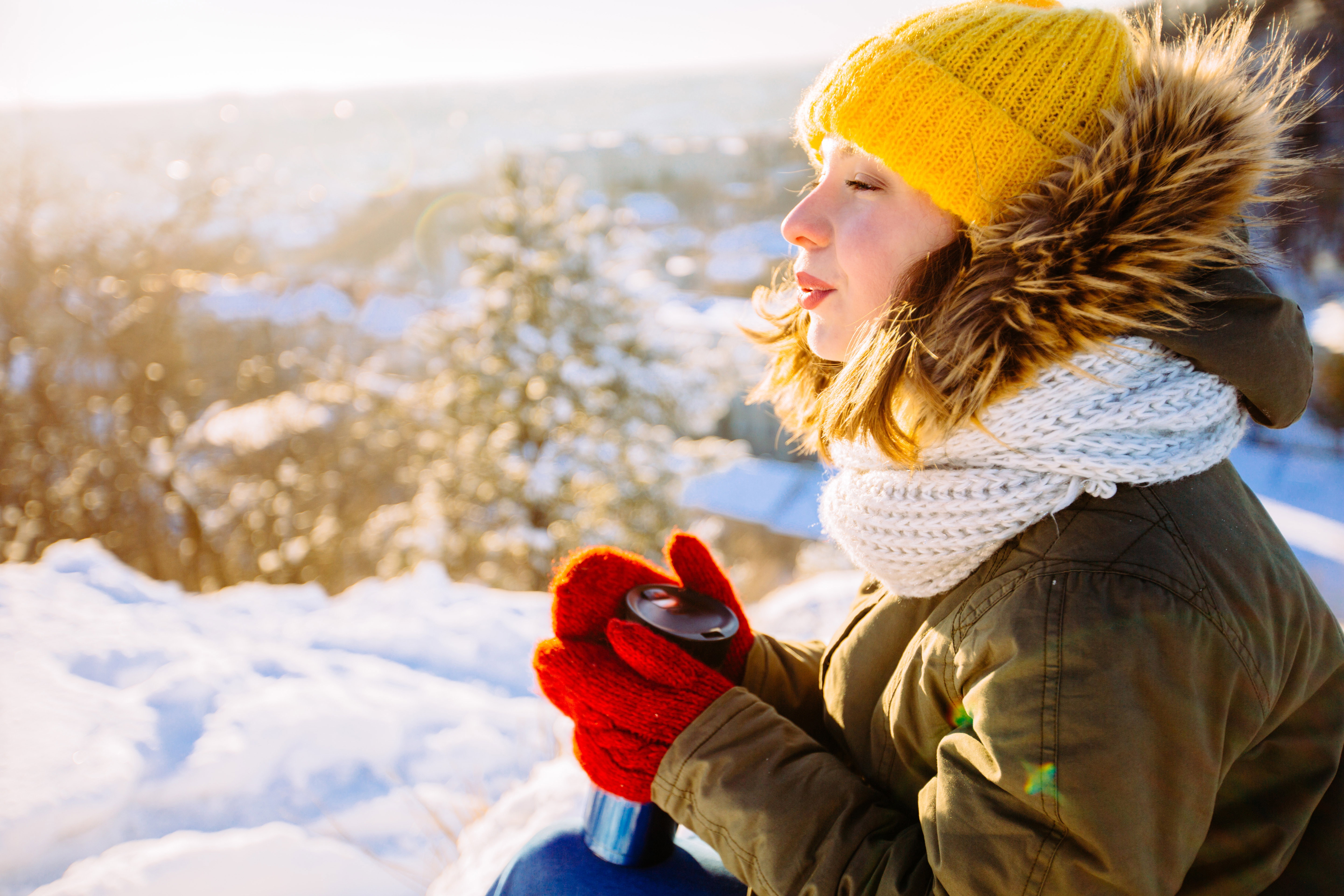 North hipster girl relaxing on the hill. Woman drinking hot tea from thermo cup and enjoing panorama city view. Happiness, winter holidays, tourism, travel and people concept.