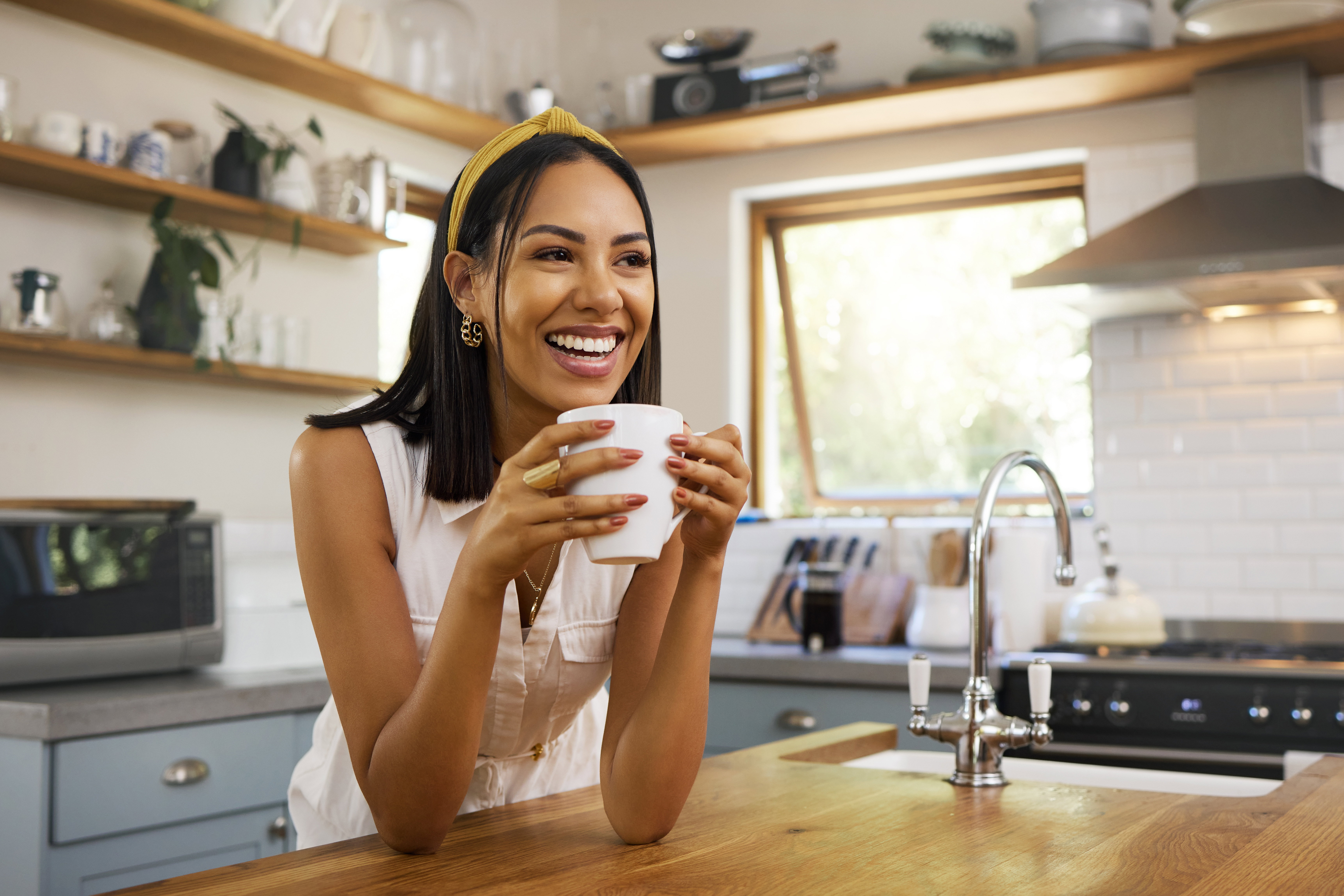 Happy woman, coffee or tea in home kitchen and relax with a smile in the morning at house. Calm young person, smiling at peace and tea drink to wake up to start day with positive joyful thoughts