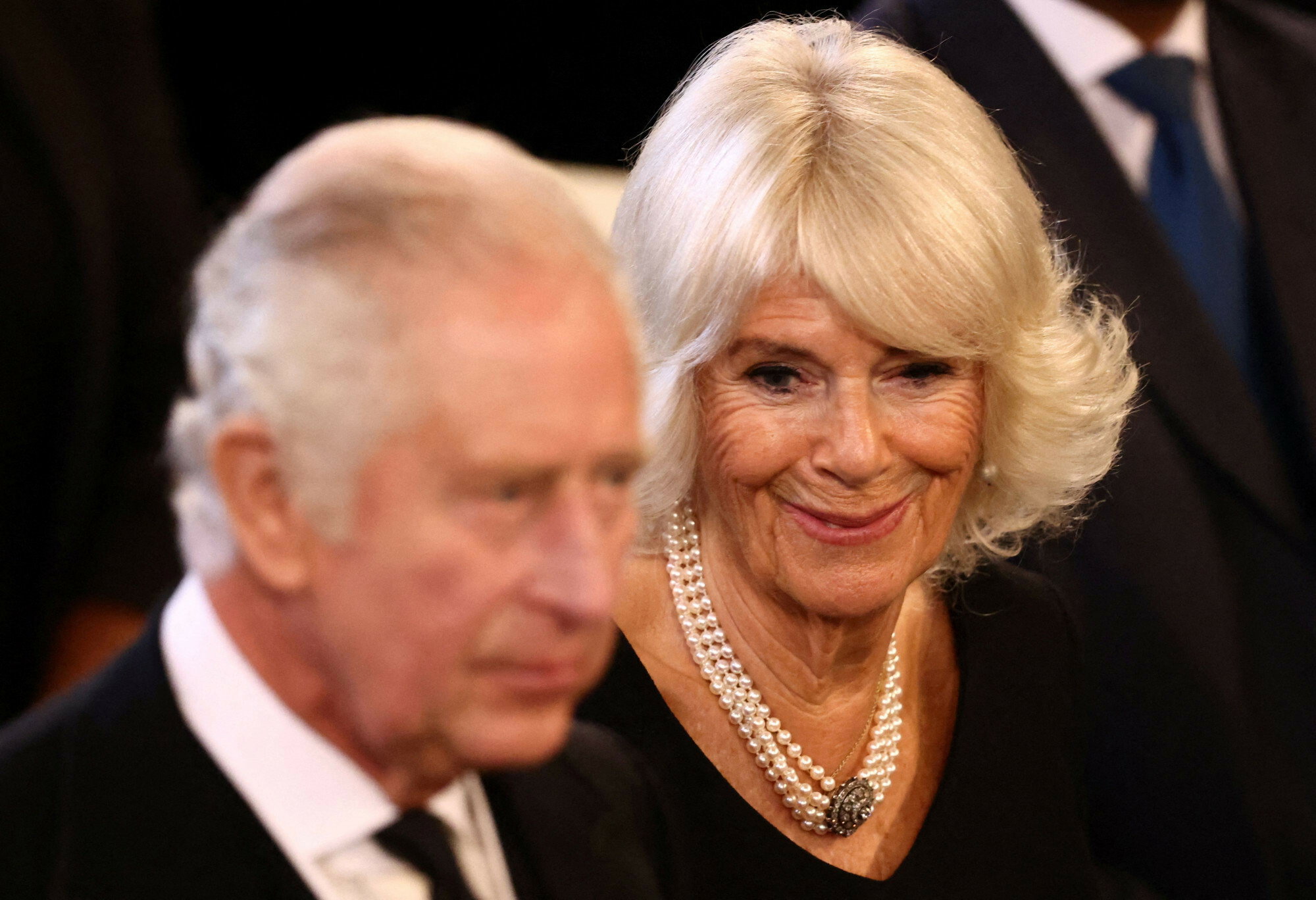 zamyślony król Karol III i uśmiechnięta Camilla