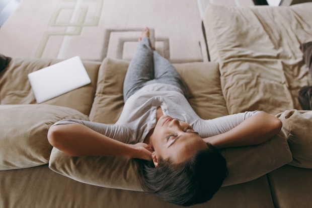 Young woman at home lying on the sofa and relaxing in her living room with her hands under her head. Close up. View from above.