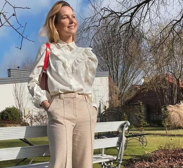 Paulina Sykut w białej letniej bluzce z falbankami i bufkami i beżowych spodniach