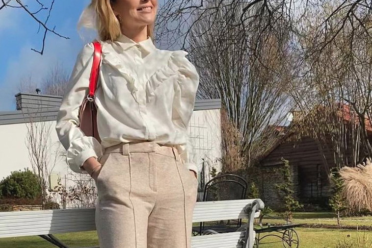 Paulina Sykut w białej letniej bluzce z falbankami i bufkami i beżowych spodniach