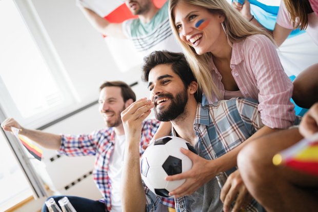 Cheerful group of friends watching football game on tv.