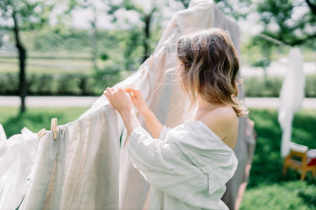 Woman Hanging Up Wet Laundry On Clothesline. The concept of unity girl with nature and the beginning of spring time with flowering trees. sunny day in village