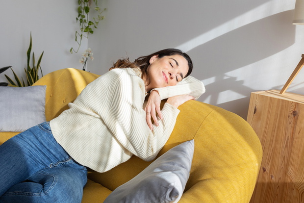 Young beautiful woman enjoying sunlight resting on sofa at home. Simple living concept