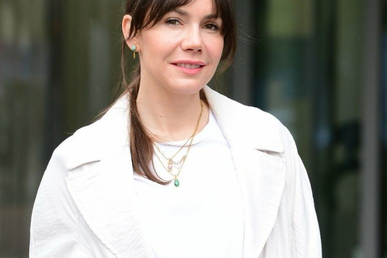 Olga Bołądź w białej bluzce i jasnym płaszczu