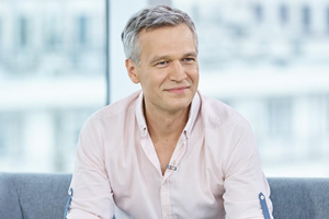 Michał Żebrowski siedzi na szarej kanapie