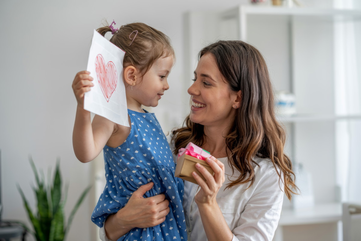 A little girl gives her mom a heart-shaped drawing and a gift box for Mother's Day.